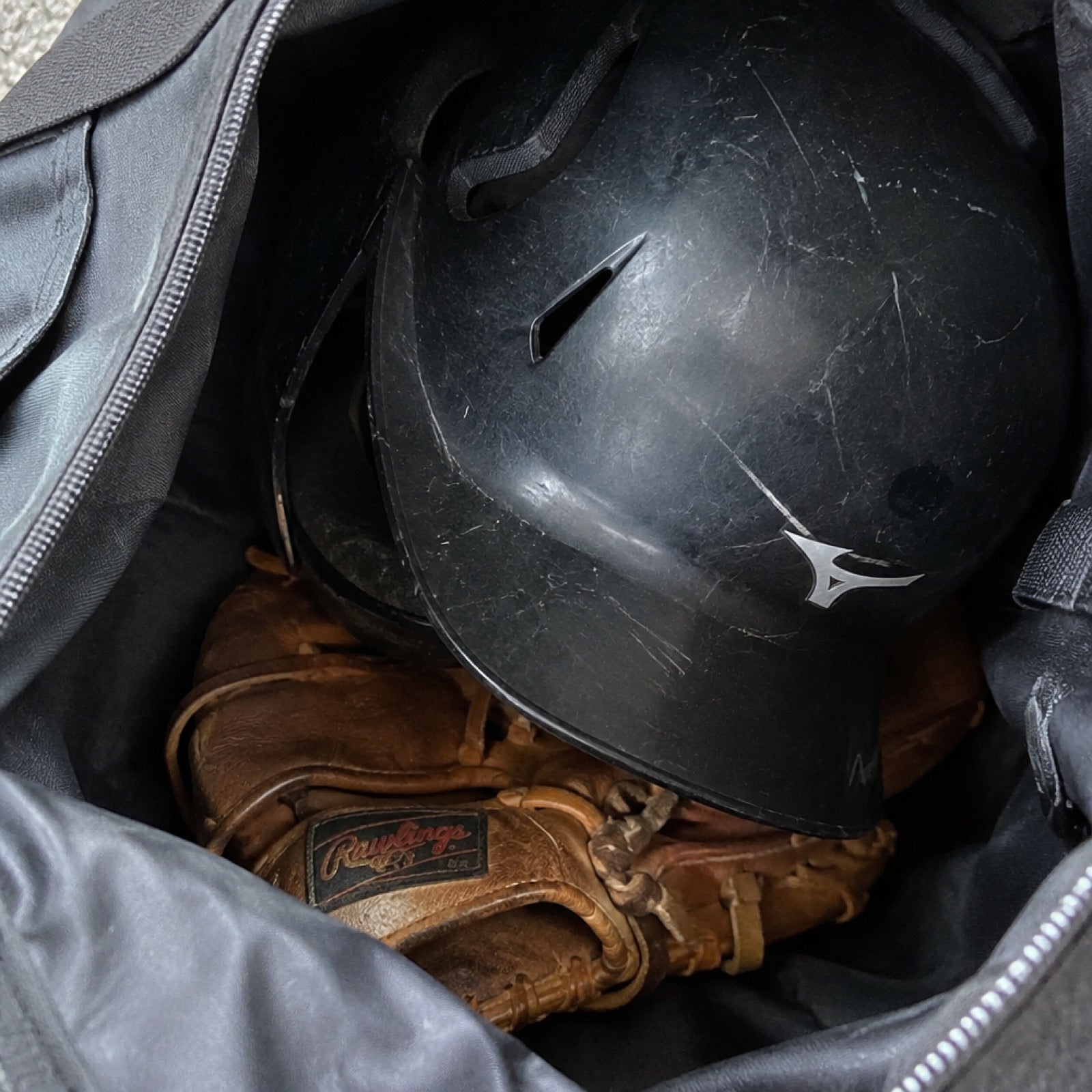 A glove crushed under a batting helmet at the bottom of a bag